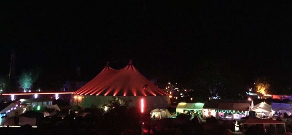 Nachtaufnahme über das Chaos Communication Camp von 2019, in der Mitte steht ein bunt beleuchtetes Zirkuszelt