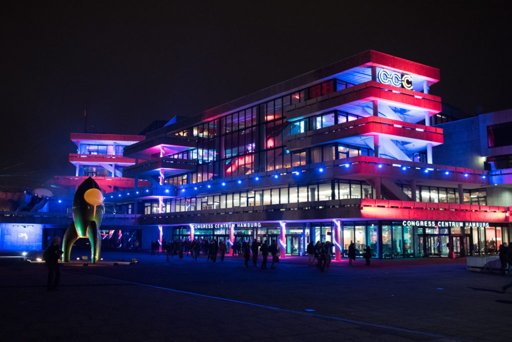 Das Congress Centrum Hamburg bei Nacht und bunt beleuchtet. Auf der linken Seite sieht man die Rakete des CCC Fairydust. Hier wird der 37c3 stattfinden.